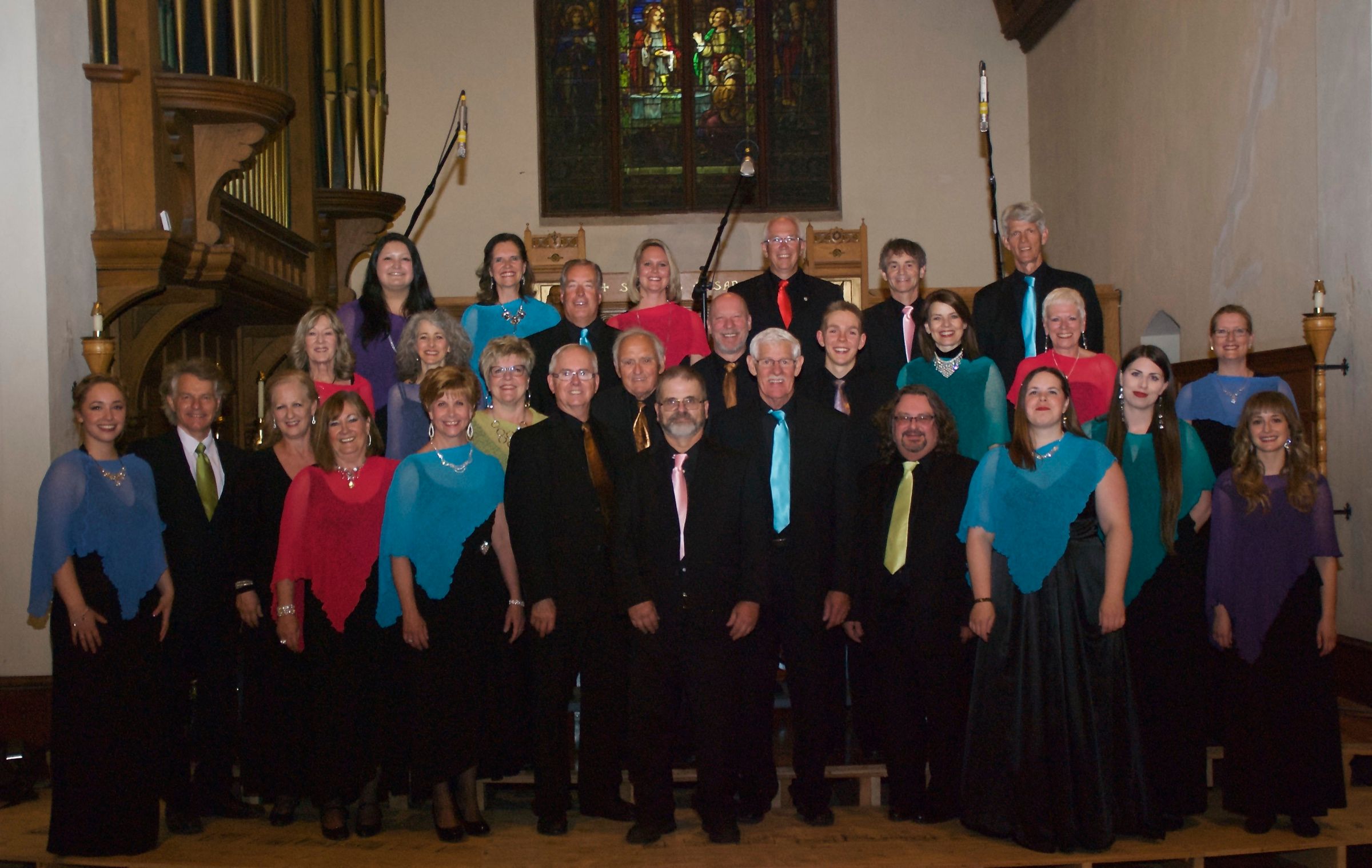 The choir posed in rows on the chancel before the organ pipes and a stained-glass window, the women in black with shawls of blue, teal, red, lilac and gold, the men in black suits with coloured ties.