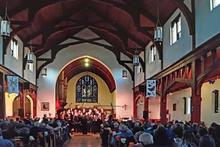 The choir on the steps at the far end of St Michael's Cathedral, beneath the stained-glass window and the beamed roof, with a full house in the pews.