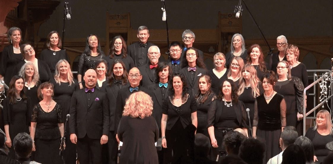 The full Spectrum Singers choir on risers in concert dress, with Kim Kleineberg conducting in the foreground.